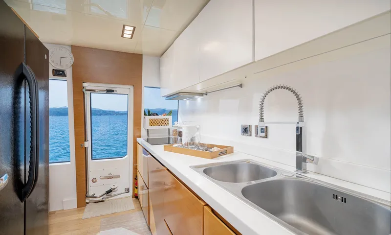 Enjoy I: Cozinha com pia dupla de aço, armários brancos, geladeira alta e porta lateral para o mar