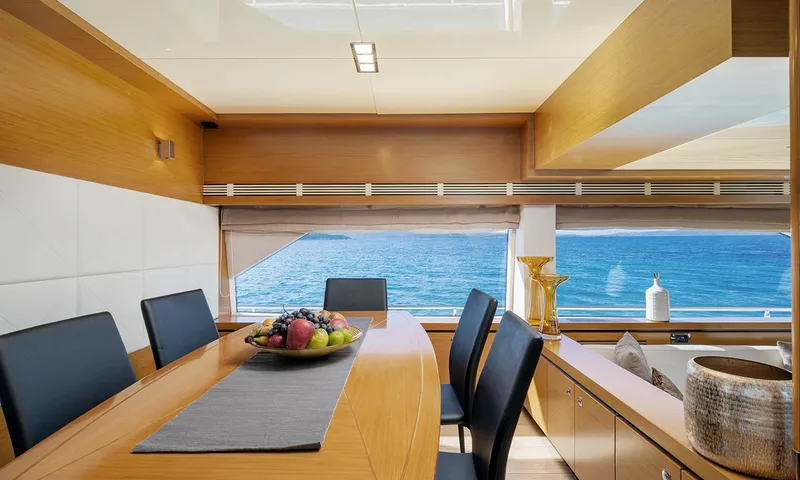 Enjoy I: Mesa de jantar interna com fruteira e cadeiras escuras ao lado de grandes janelas com vista para o mar