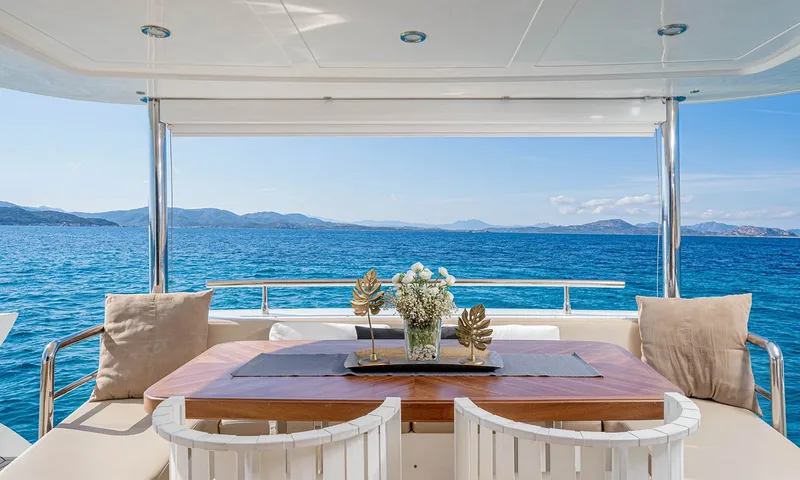 Enjoy I: Mesa de jantar do convés de popa com flores e cadeiras brancas, com vista para o mar azul e as colinas