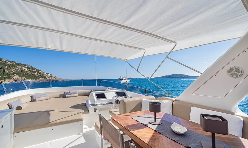Enjoy I: Flybridge com sombra, posto de comando, assentos no colchonete de sol e mesa de madeira voltada para o mar