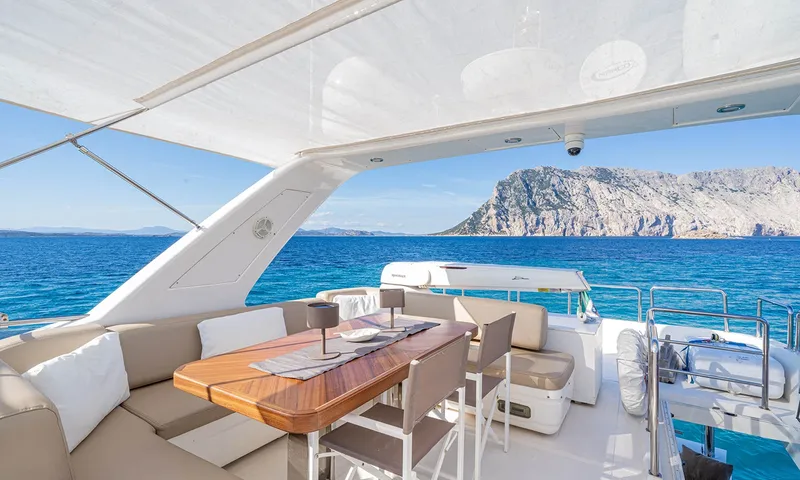 Enjoy I: Mesa de jantar e lounge do flybridge sob uma cobertura, com uma ilha rochosa à vista