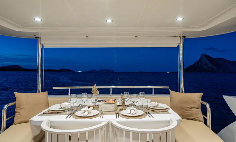 Enjoy I: Mesa do convés de popa posta para o jantar à noite, com mar escuro e colinas ao fundo