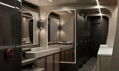 HYP3: Dim washroom with twin basins, illuminated mirrors and a row of dark stall doors