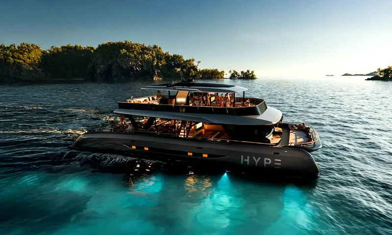 HYP3: Catamaran cruising at dusk with guests on both decks and lights glowing beneath the hull