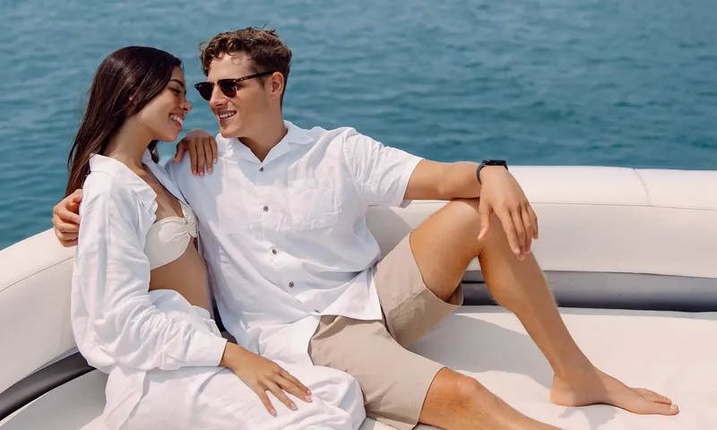 HYP3: Smiling couple in white clothes sitting together on cushioned deck seating by the sea