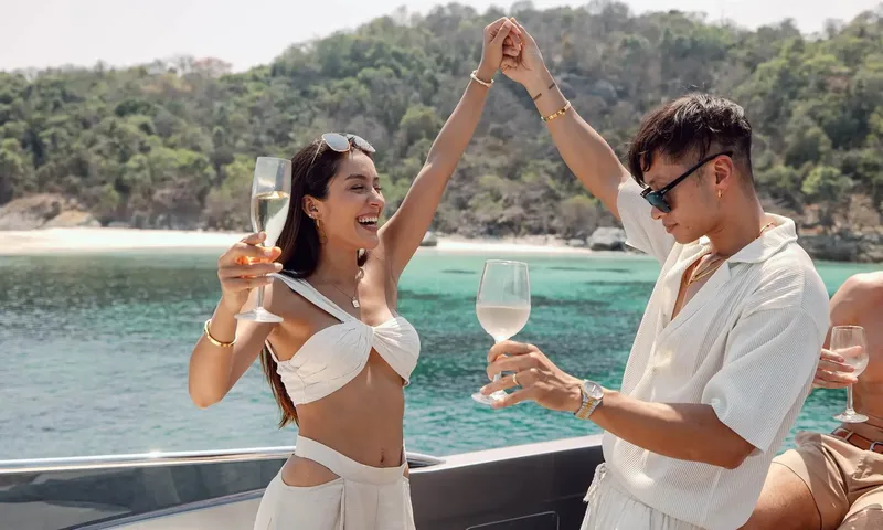 HYP3: Couple holding wine glasses dancing on deck with a green hillside and beach behind