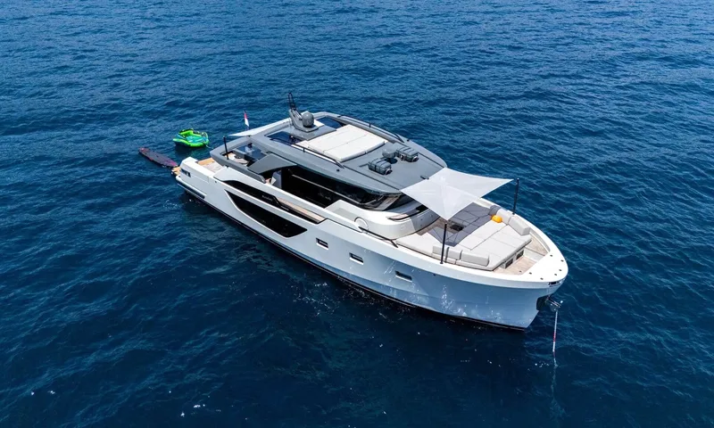 Jamon: Aerial view of the yacht at anchor in deep blue water with an inflatable towable astern