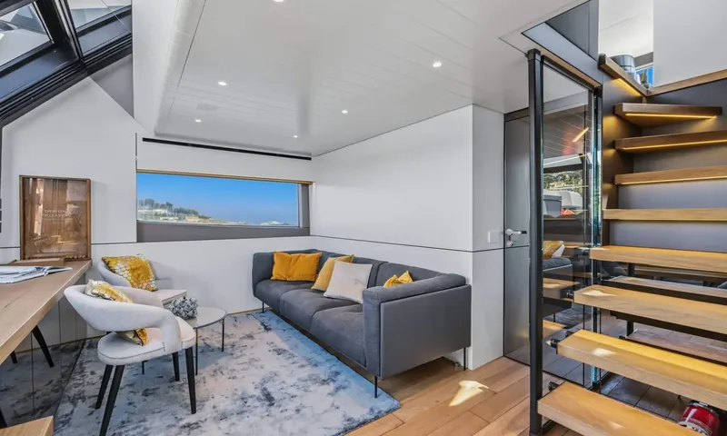 Jamon: Lounge with grey sofa, rug, armchairs and lit floating wooden stairs