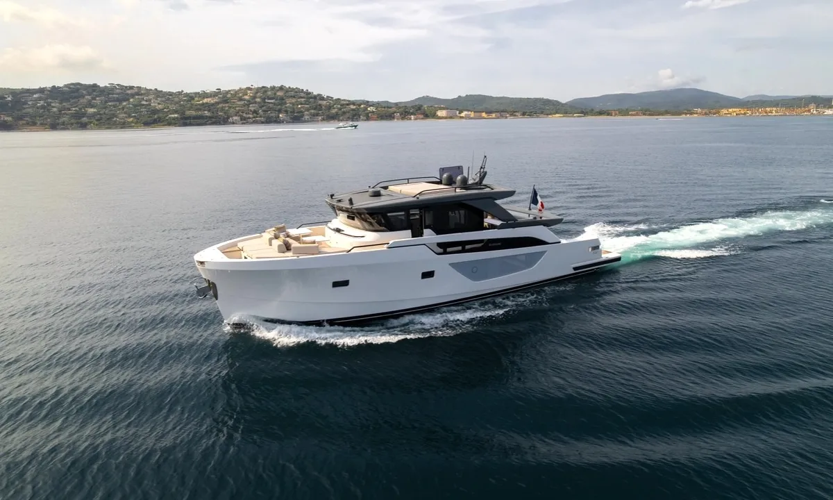 CC: White motor yacht cruising across calm blue water with green hills and coastline behind