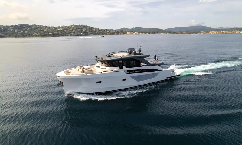 CC: White motor yacht cruising across calm blue water with green hills and coastline behind