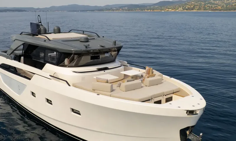 CC: Elevated view of the yacht bow with cushioned foredeck lounge on calm blue water