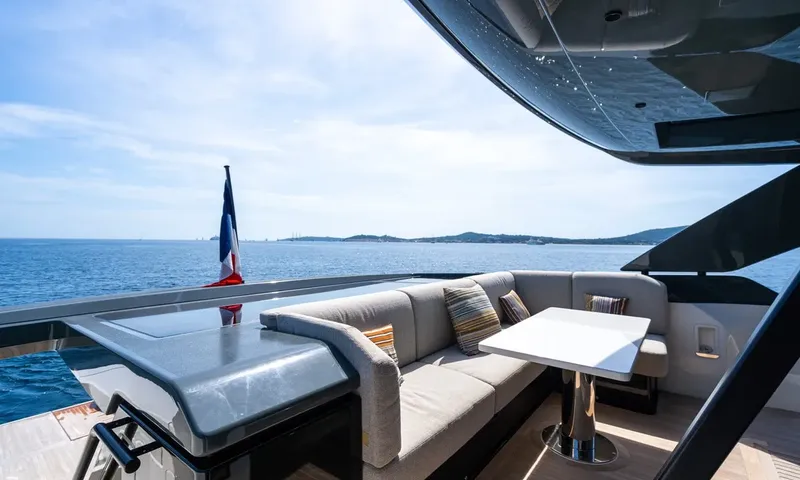 CC: Shaded aft deck sofa with a small table and flag, sea and island behind