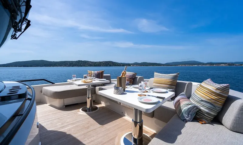 CC: Two set tables with sofa seating and striped cushions on a sunny deck facing the coast