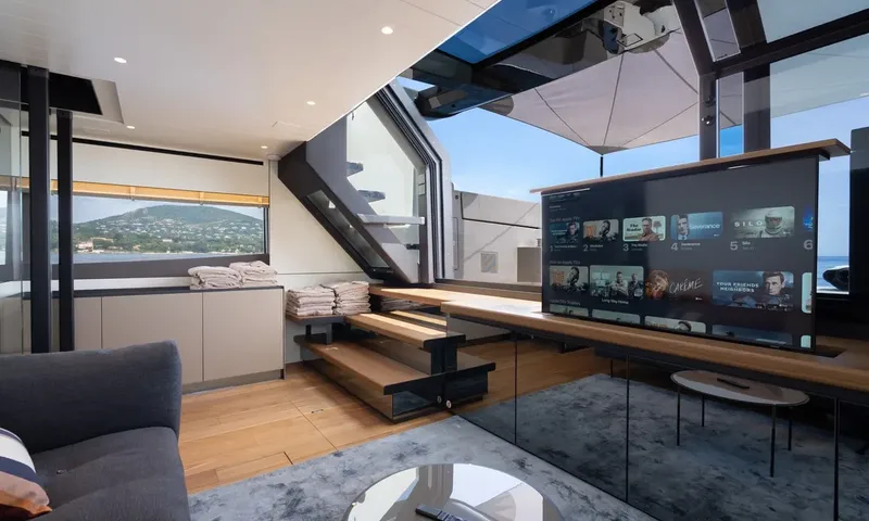 CC: Lounge with sofa, large pop up television, wooden stairs and folded towels by windows