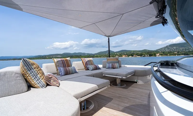CC: Shaded outdoor lounge with striped cushions under a sail canopy facing green hills