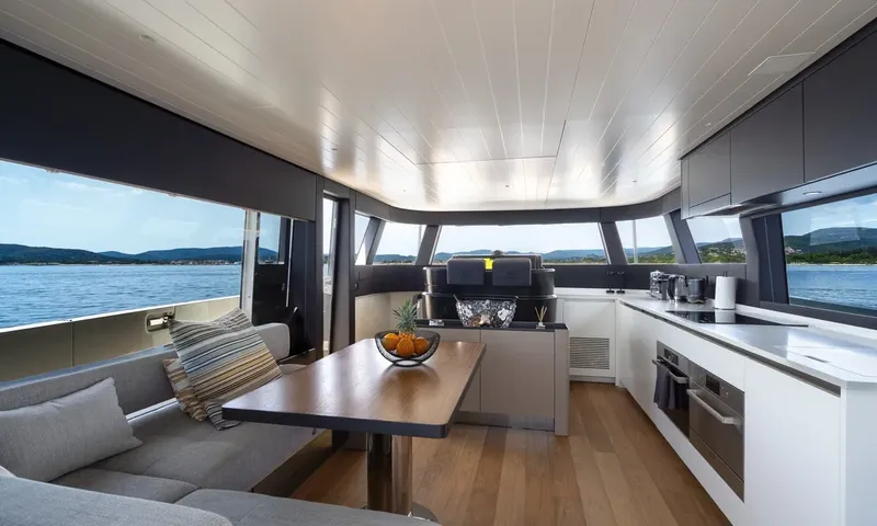 CC: Main deck with dining table, sofa, open galley and wide windows onto the sea