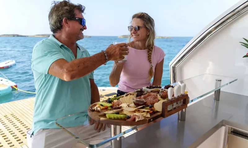 Louder: Couple toasting at a glass bar with a grazing board, water toys floating behind