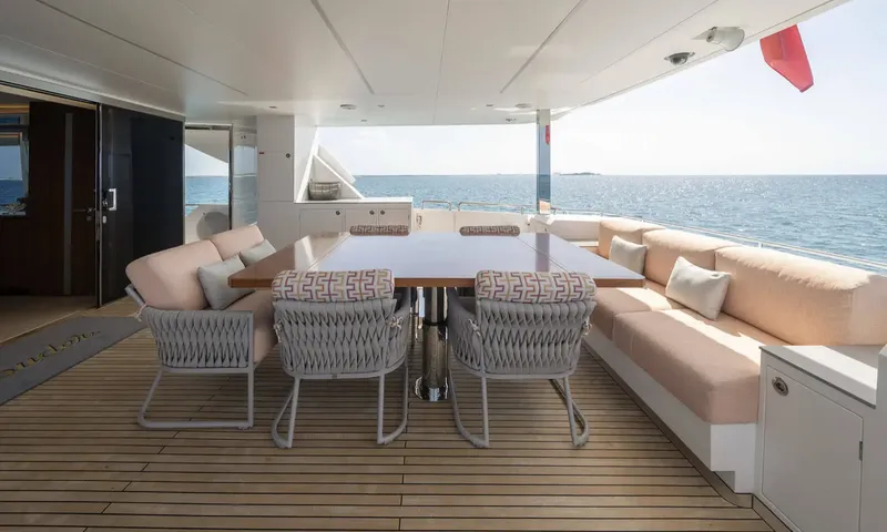 Louder: Covered aft deck dining table with woven chairs and bench seating facing the sea
