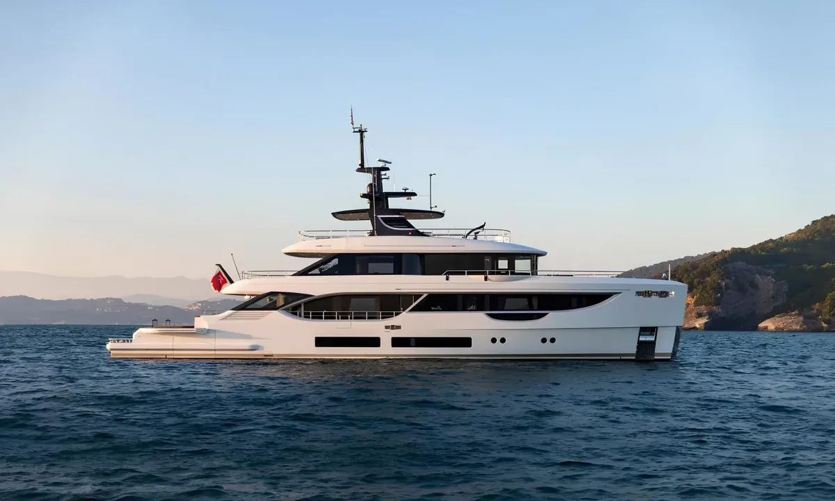 Aitana: White motor yacht at anchor in calm blue water near a green rocky coastline at dusk