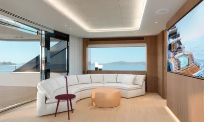 Aitana: Lounge with curved white sofa, round ottoman, large window to the sea and wall screen