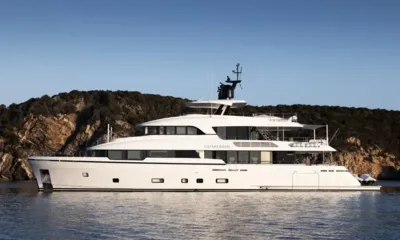Lumière: Profile view of a white yacht anchored in front of a wooded rocky hillside