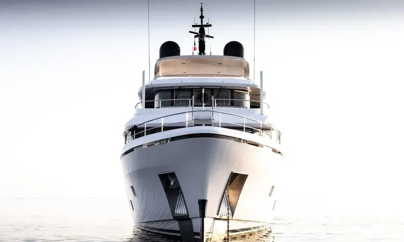 Lumière: Head on view of a white yacht bow on calm water under a pale sky