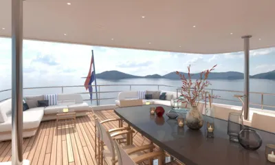 Lumière: Covered aft deck dining table with candles and vases, sofas and a flag facing the sea