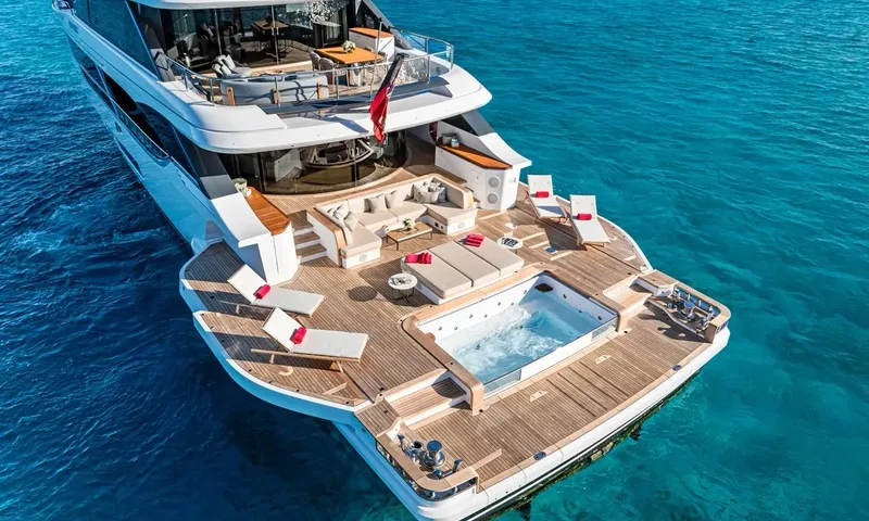 Wavė: Erhöhte Ansicht des Achterdecks mit Sofa, Sonnenpolstern, Liegen und Tauchbecken über klarem Wasser