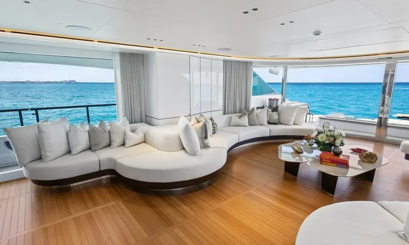 Wavė: Geschwungenes weißes Sofa und gläserner Couchtisch neben großen Fenstern zum Meer