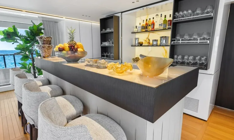Wavė: Bartresen mit gepolsterten Hockern, Obstschale und Regalen mit Gläsern und Flaschen