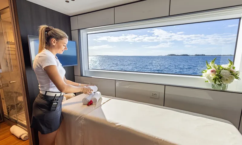 Wavė: Crewmitglied legt Handtücher auf eine Massageliege neben einem großen Fenster mit Meerblick