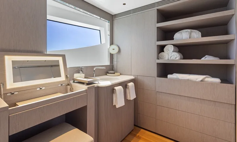 Wavė: Badezimmer mit Spiegel, Waschbecken, Handtüchern und Regalen unter einem Fenster