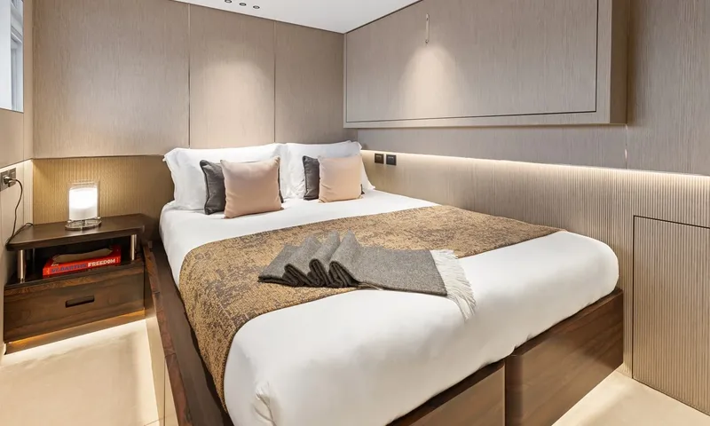 Wavė: Doppelbett mit gemustertem Überwurf und gefalteter Decke in einer Kabine mit sanft beleuchteten Paneelen