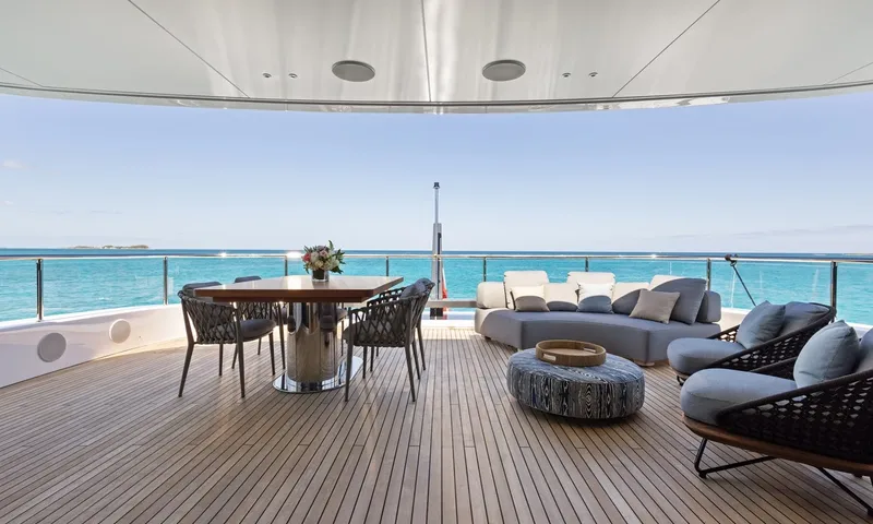 Wavė: Schattiges Achterdeck mit Esstisch, geschwungenem Sofa und Sesseln mit Blick auf türkisfarbenes Meer