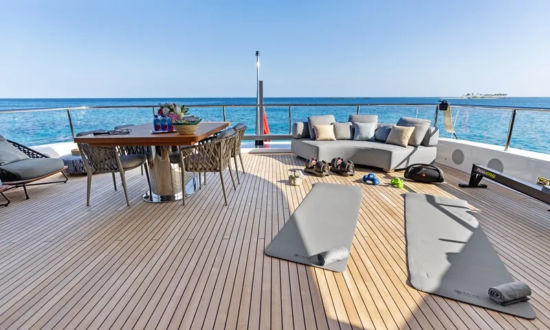 Wavė: Teakdeck mit Yogamatten, Hanteln und Rudergerät neben einem Tisch und Sofa