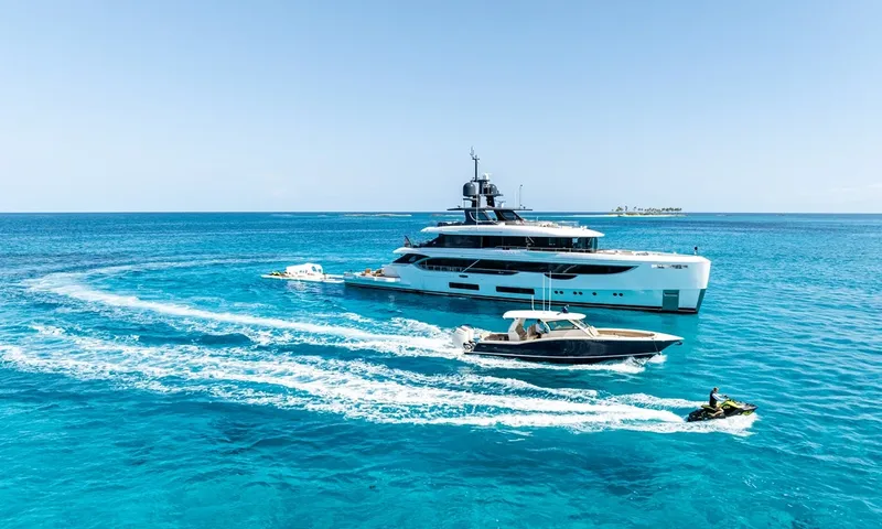 Wavė: Yacht in klarem blauem Wasser mit einem Tender und einem vorbeirasenden Jetski