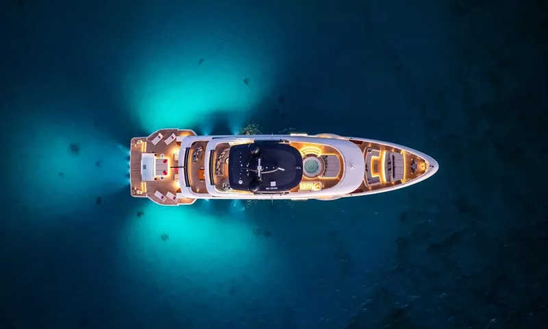 Wavė: Draufsicht bei Nacht auf die beleuchtete Yacht mit leuchtenden türkisfarbenen Unterwasserlichtern