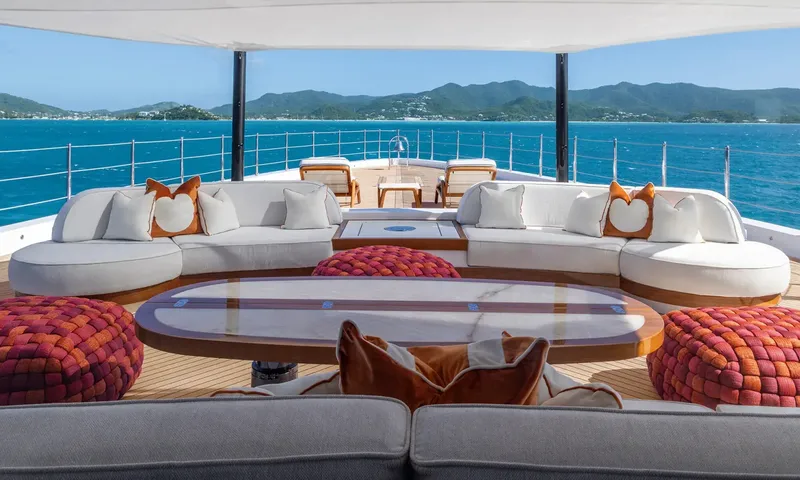 Amor à Vida: Shaded deck lounge with curved white sofas, oval table and woven poufs facing green hills