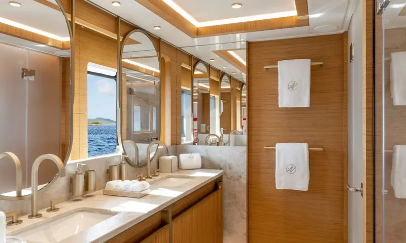 Amor à Vida: Wood and marble bathroom with double sinks, round mirrors and a sea view window