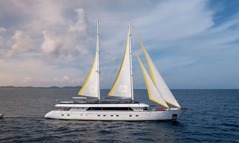 Anima Maris: Two masted yacht under full sail with yellow trimmed sails on calm sea