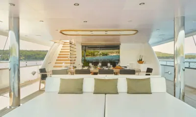Anima Maris: Covered aft deck with a large sunpad in front of a set dining table and staircase