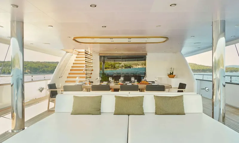Anima Maris: Covered aft deck with a large sunpad in front of a set dining table and staircase