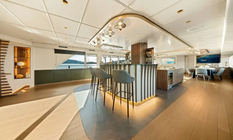 Anima Maris: Curved bar with upholstered stools and a dining area beyond in a bright saloon