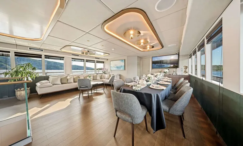 Anima Maris: Indoor dining table set for guests with a sofa lounge and windows behind