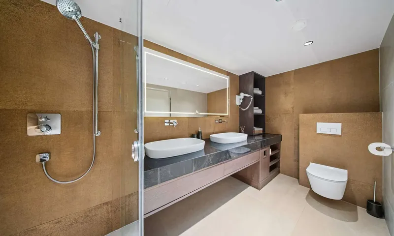 Anima Maris: Bathroom with twin sinks on dark stone counter, lit mirror, shower and toilet