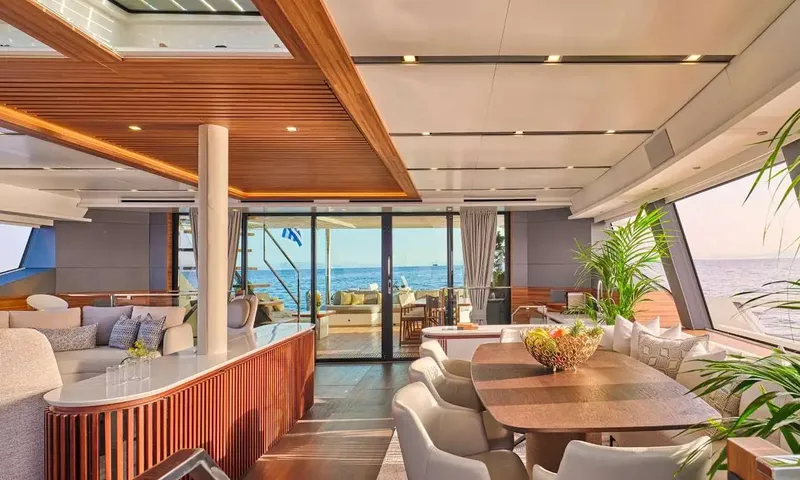 Alina: Open saloon with dining table, bar counter and wood ceiling, glass doors open to the aft deck