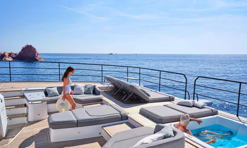 Alina: Foredeck lounge with grey sunpads and a man relaxing in a jacuzzi beside a woman
