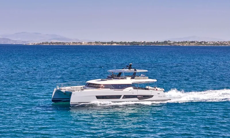 Alina: White power catamaran cruising across blue sea with a low coastline in the distance