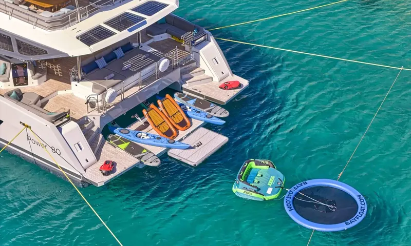 Alina: Stern of catamaran with kayaks, paddleboards, floating mat, tube and trampoline in turquoise water