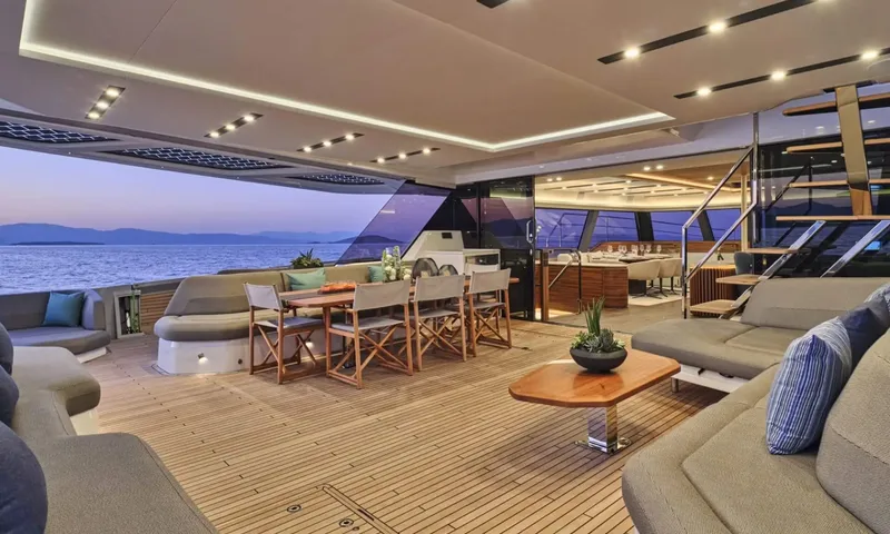Alina: Aft deck at dusk with dining table, sofas and coffee table, saloon visible through glass